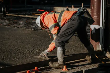 Ein Bauarbeiter in leuchtender Weste glättet frischen Beton auf einer Baustelle.